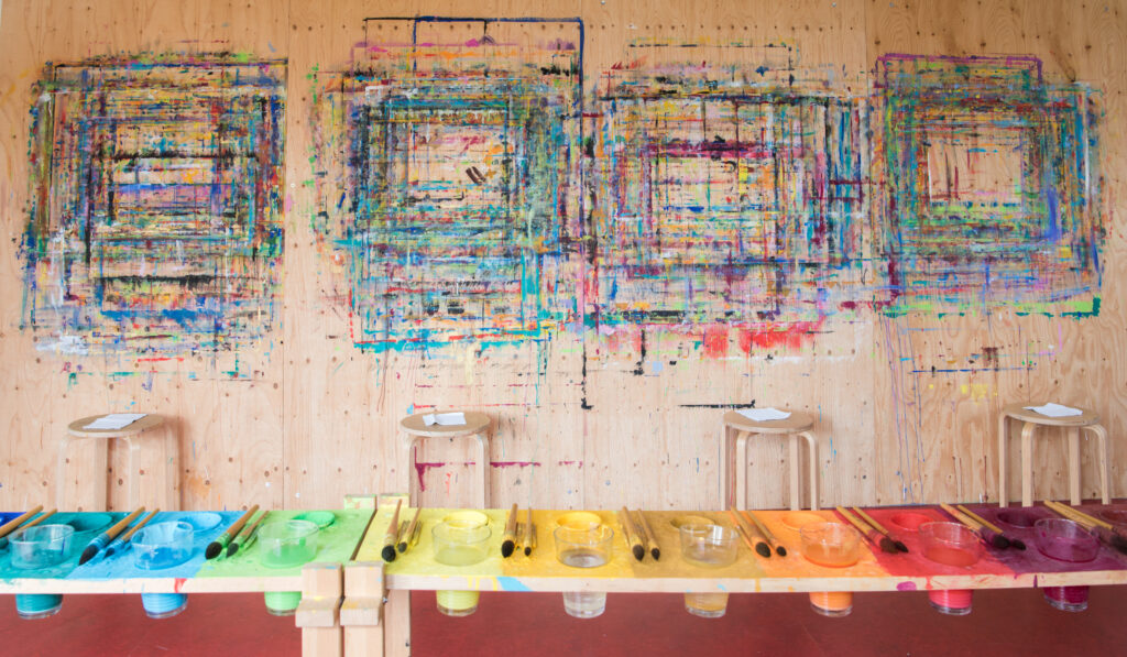 Blick auf Holzwand mit Malspuren, davor eine Palette mit Farben