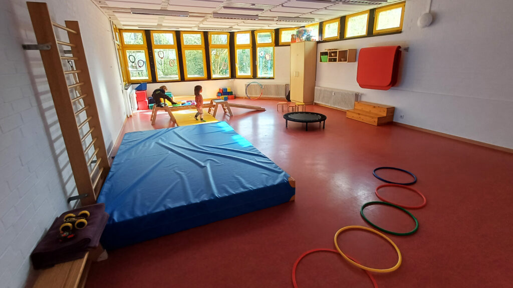 In einer Turnhalle sieht man verschiedene Geräte aufgebaut und zwei Kinder beim spielen.